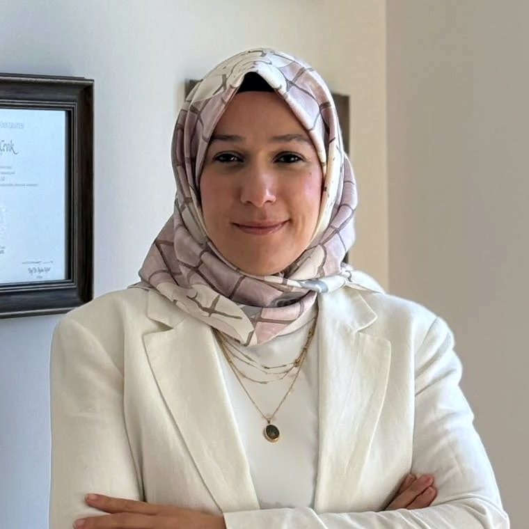 Huriye Çevik, diplomalarının asılı olduğu duvarın önünde gülümsüyor